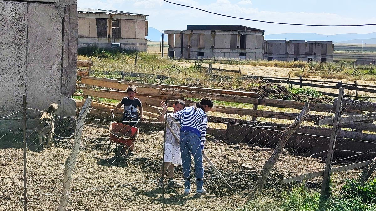 Kinder bei der Arbeit auf einem Bauernhof mit ländlichen Häusern und Rohbauten im Hintergrund im Dorf Apnia nahe Wardsia, Georgien