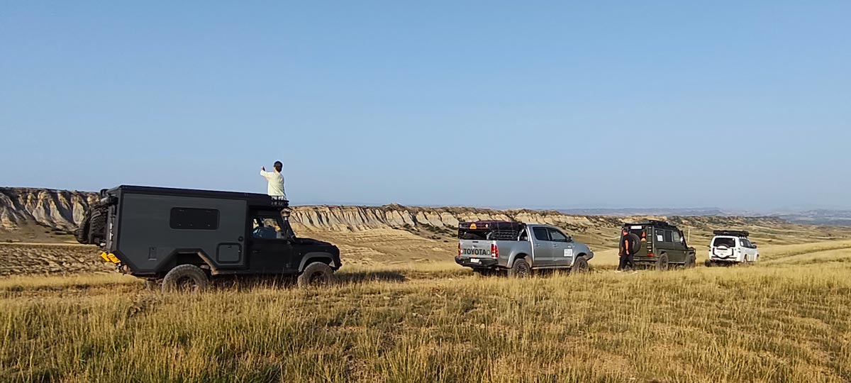 Overland-Expeditionskonvoi geparkt auf einem grasbewachsenen Kamm in der Halbwüstenlandschaft von Chalaubani, Georgien
