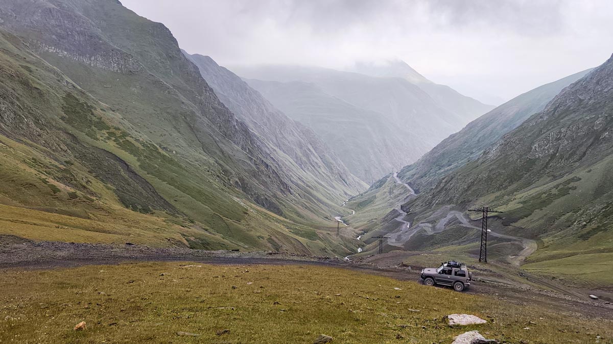 Ein Offroad-Fahrzeug mit Blick auf die dramatischen Serpentinen und weiten grünen Täler des Nordabhangs am Abano-Pass im Kaukasus, Georgien