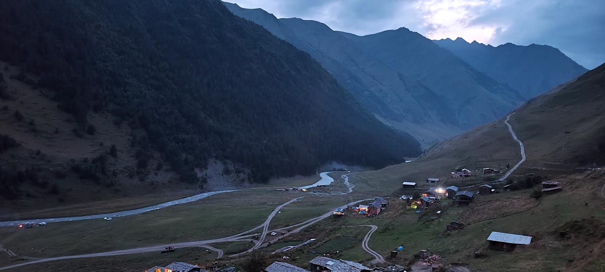 Abenddämmerungsblick auf das historische Bergdorf Dartlo mit warm leuchtenden Lichtern in einem tiefen Flusstal in Tuschetien, Georgien
