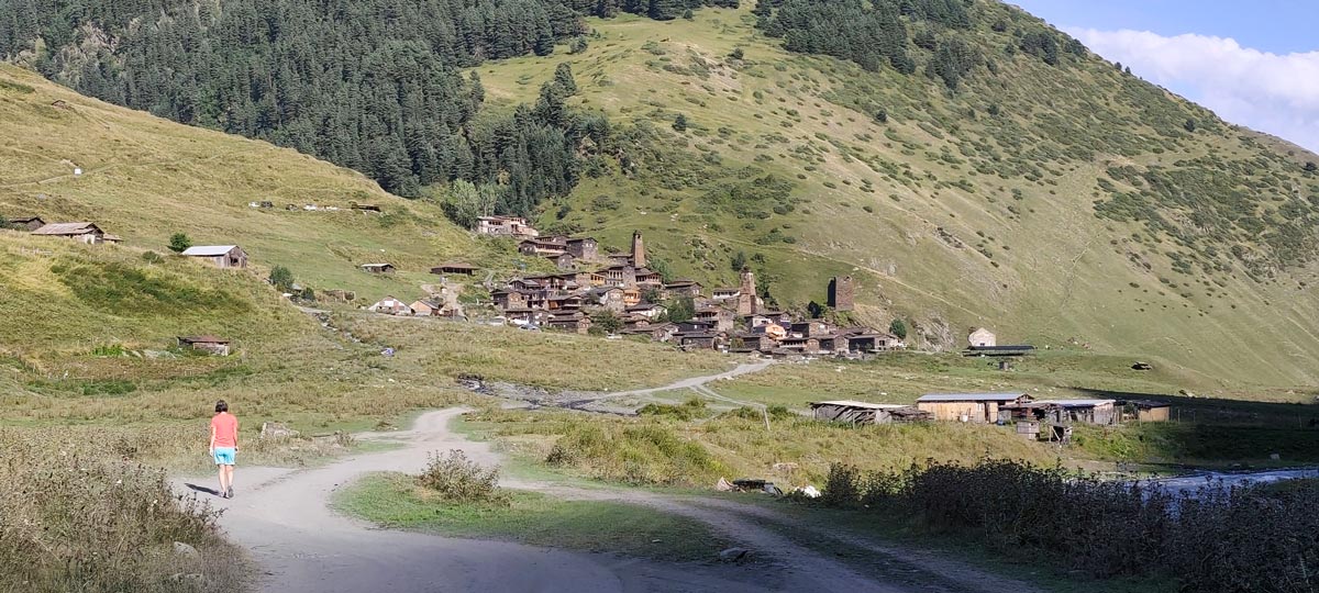Eine Person geht auf einem Feldweg in Richtung der historischen Steintürme und Häuser des Dorfes Dartlo in Tuschetien, Georgien