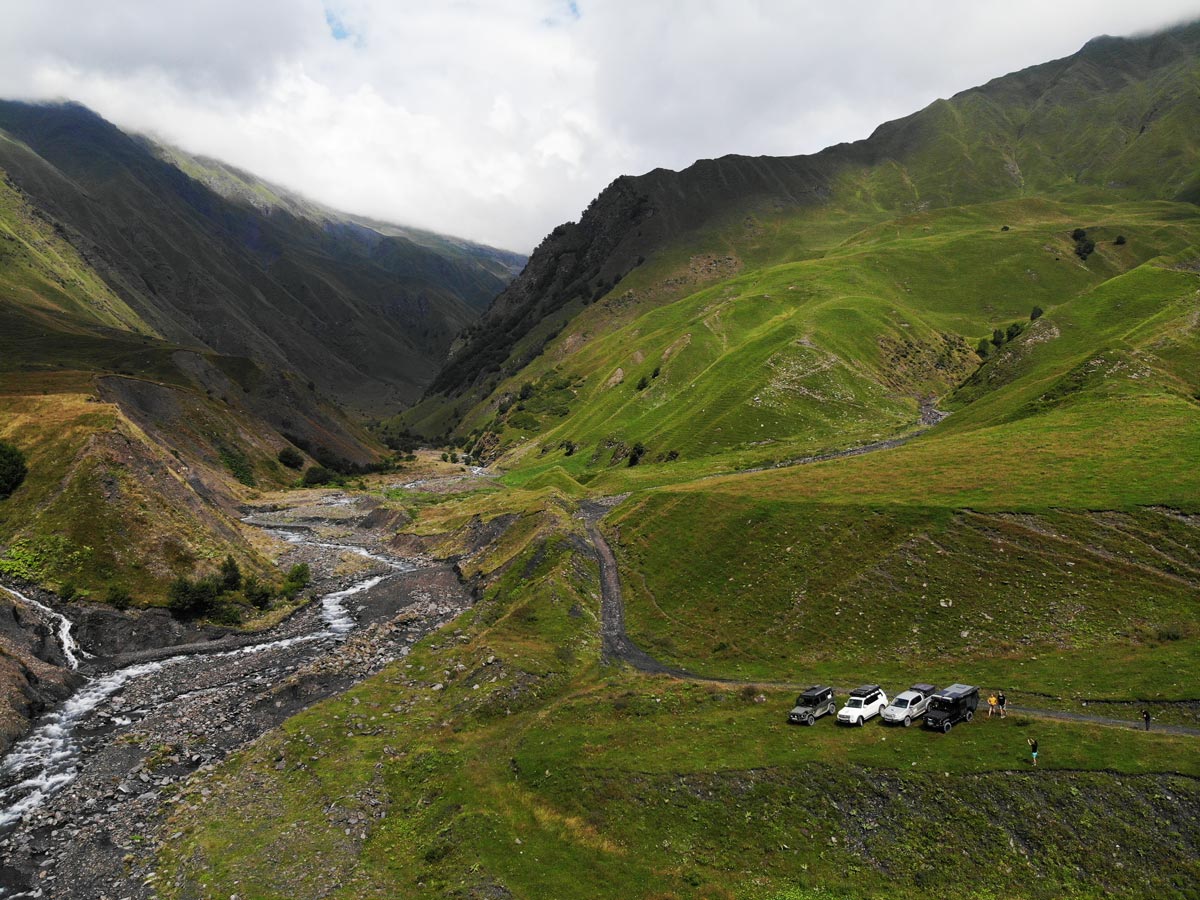 Luftaufnahme von Overland-Fahrzeugen, die am Fluss Gudamakari Aragwi in einem grünen Bergertal in Georgien geparkt sind