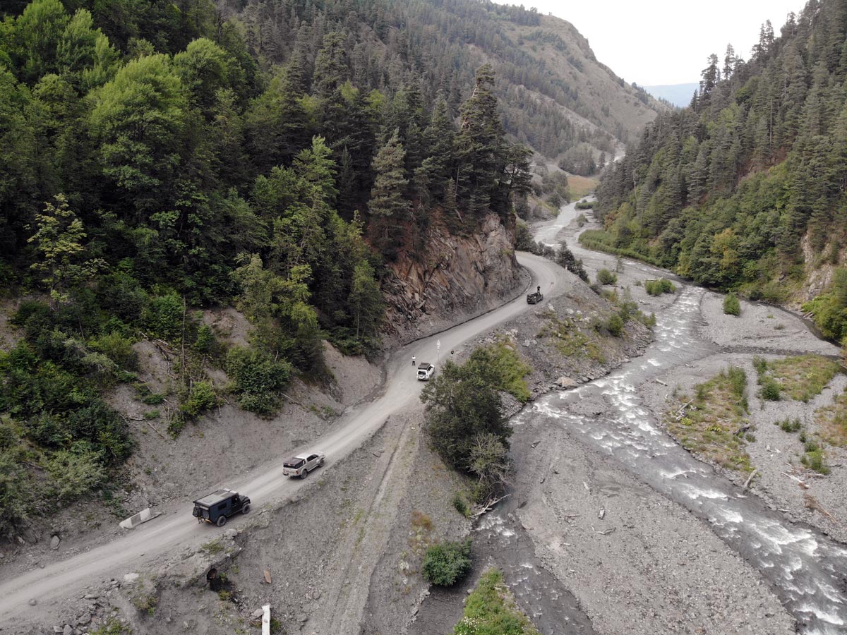 Luftaufnahme eines Expeditionskonvois auf der windungsreichen Schotterstraße zum Abano-Pass neben einer Flussschlucht in Tuschetien, Georgien