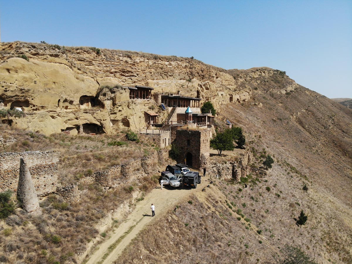 Luftaufnahme von Expeditionsfahrzeugen am historischen Höhlenkloster Natlismtsemeli in der Halbwüstenlandschaft von Kachetien, Georgien