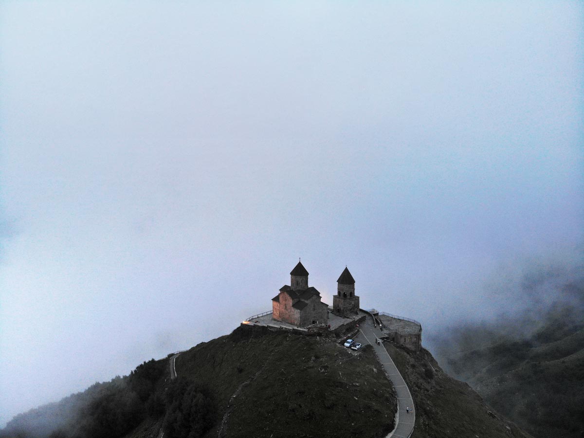 Luftaufnahme der historischen Gergetier Dreifaltigkeitskirche, umgeben von Nebel hoch oben im Kaukasusgebirge in Georgien